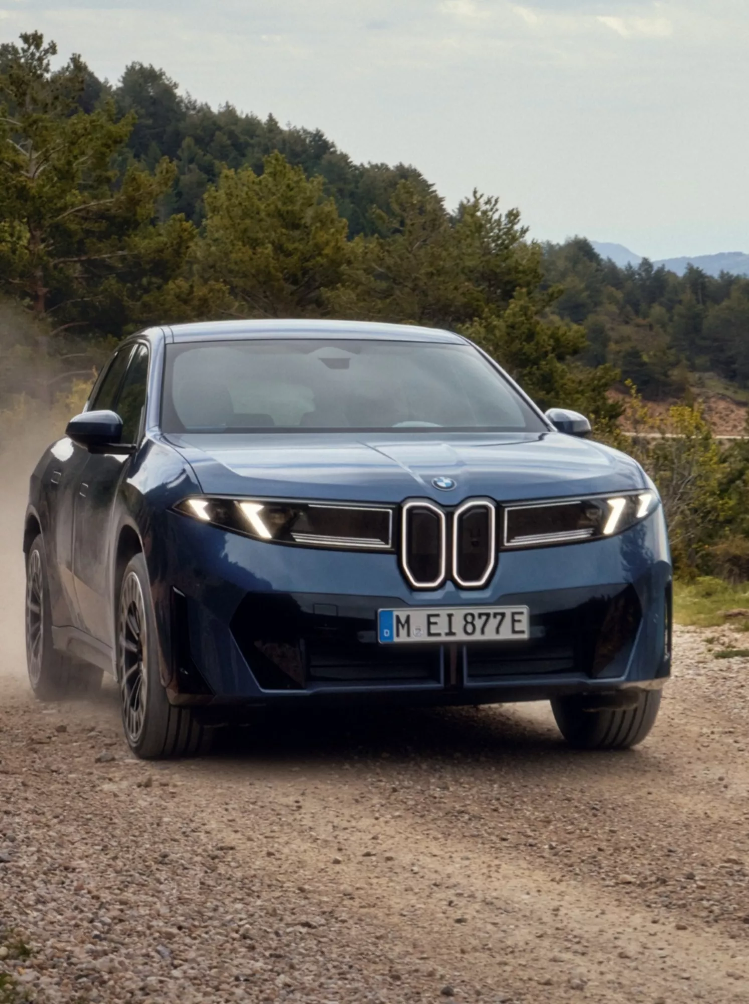 A BMW iX1 and iX2 on a mountain road in front of a wooden hut
